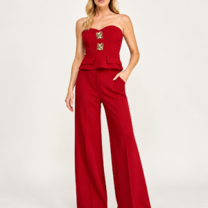 Model wearing a red strapless pant set with gold-tone front details and wide-leg trousers